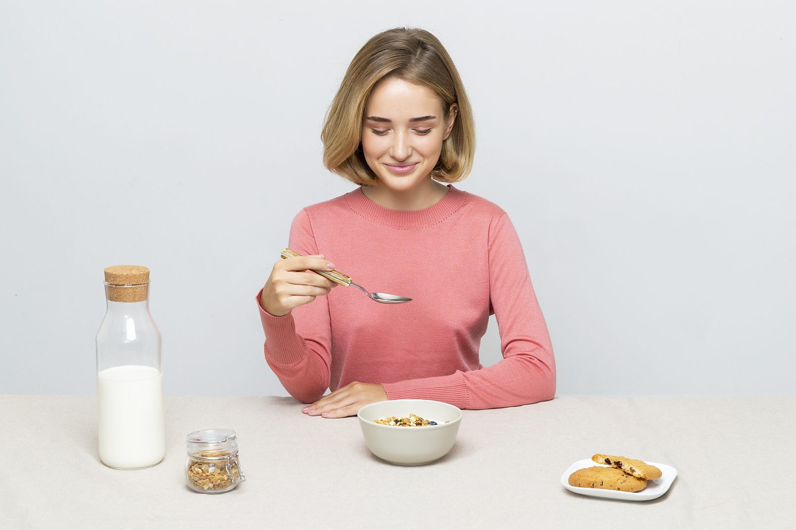 World milk day 2021: girl in a pink sweater eating muesli. There is a bottle of milk nearby