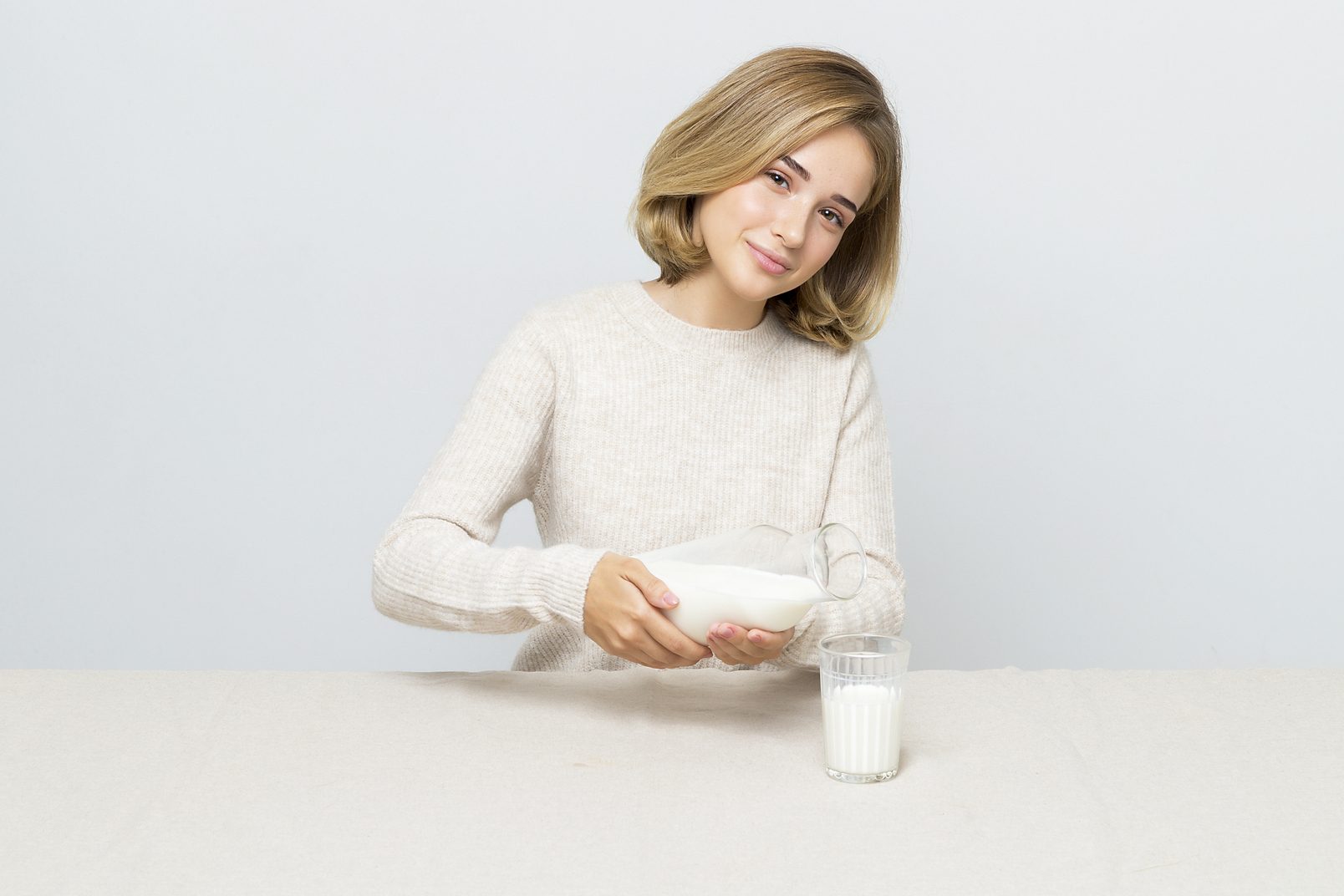 World milk day 2021: a girl in a light gray sweater sits at the table and pours milk into a glass