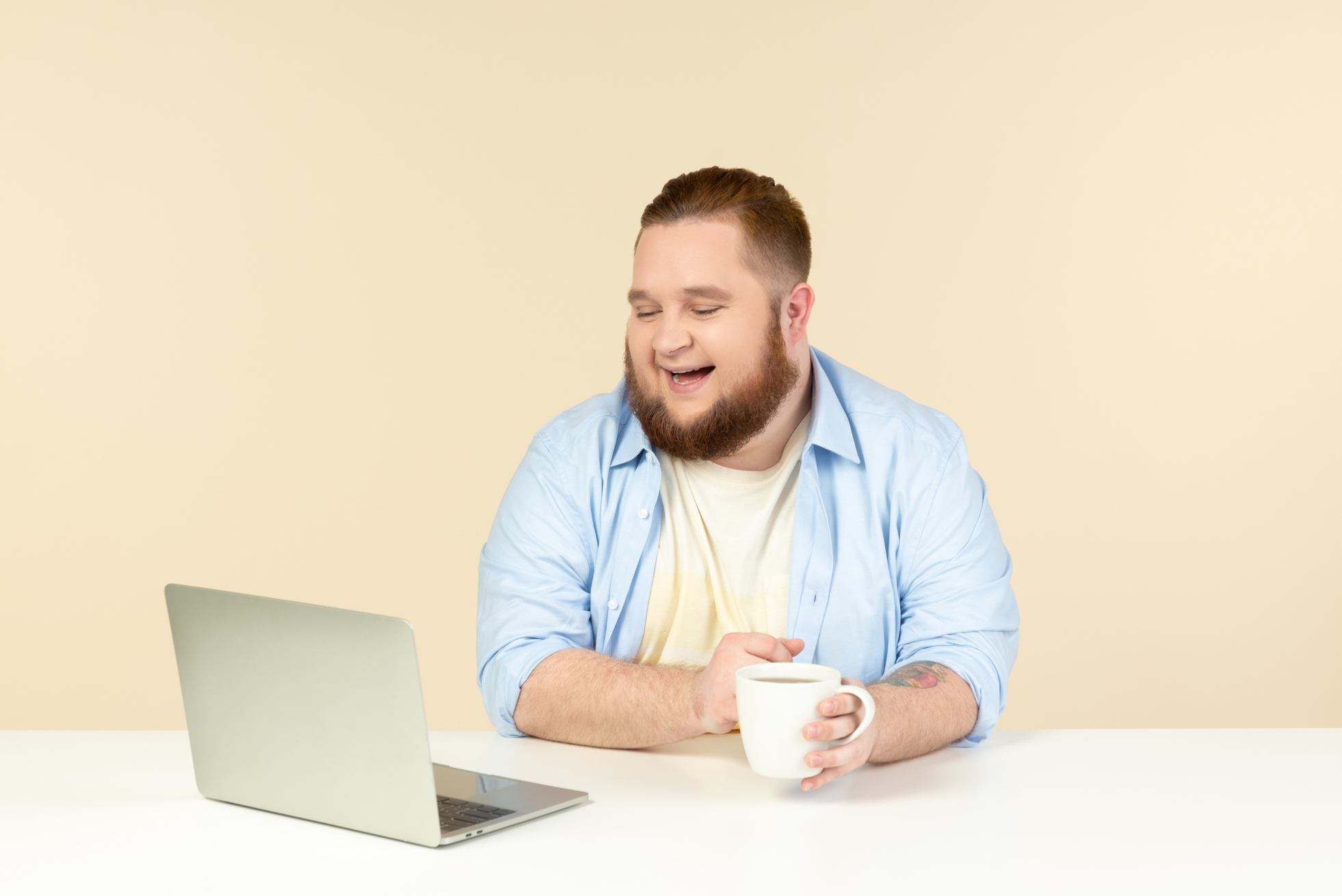 Photo of a laughing young overweight man looking at laptop and having tea