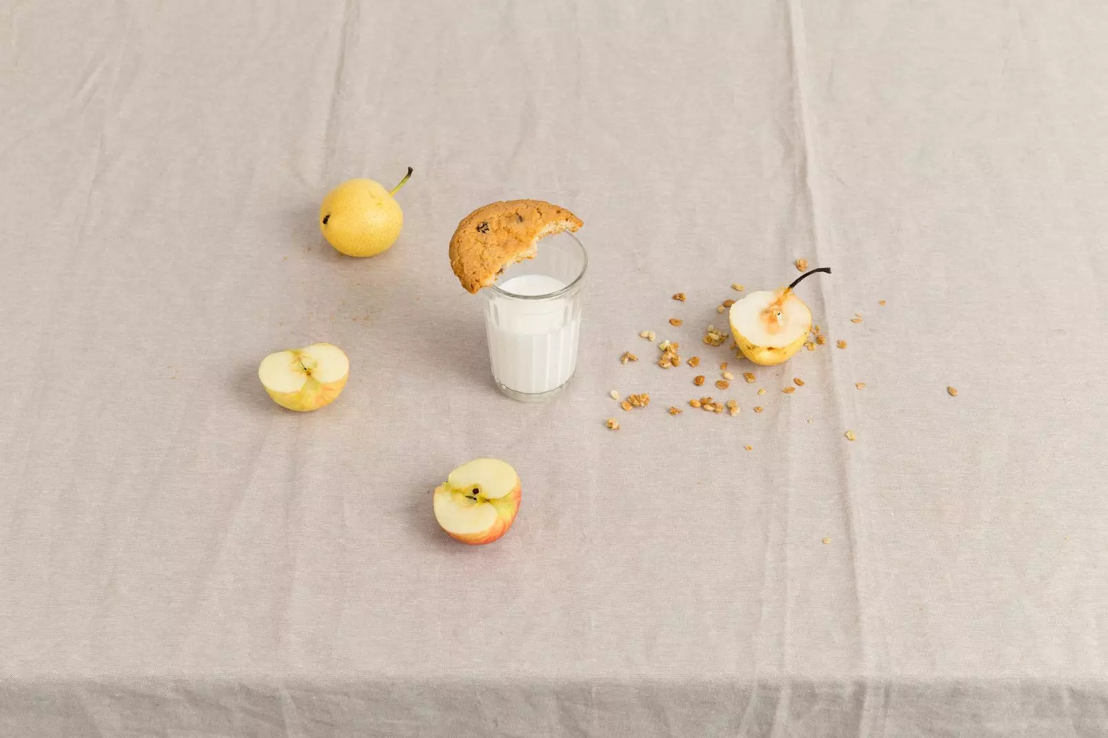 World milk day 2021: there is a glass of milk on the table, and a bitten cookie on the glass. Apples and cereals lie nearby